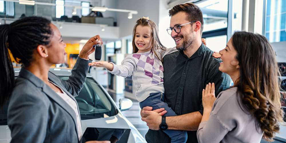 Familia sonriente recibiendo la llave de un carro en un showroom; imagen ilustrativa